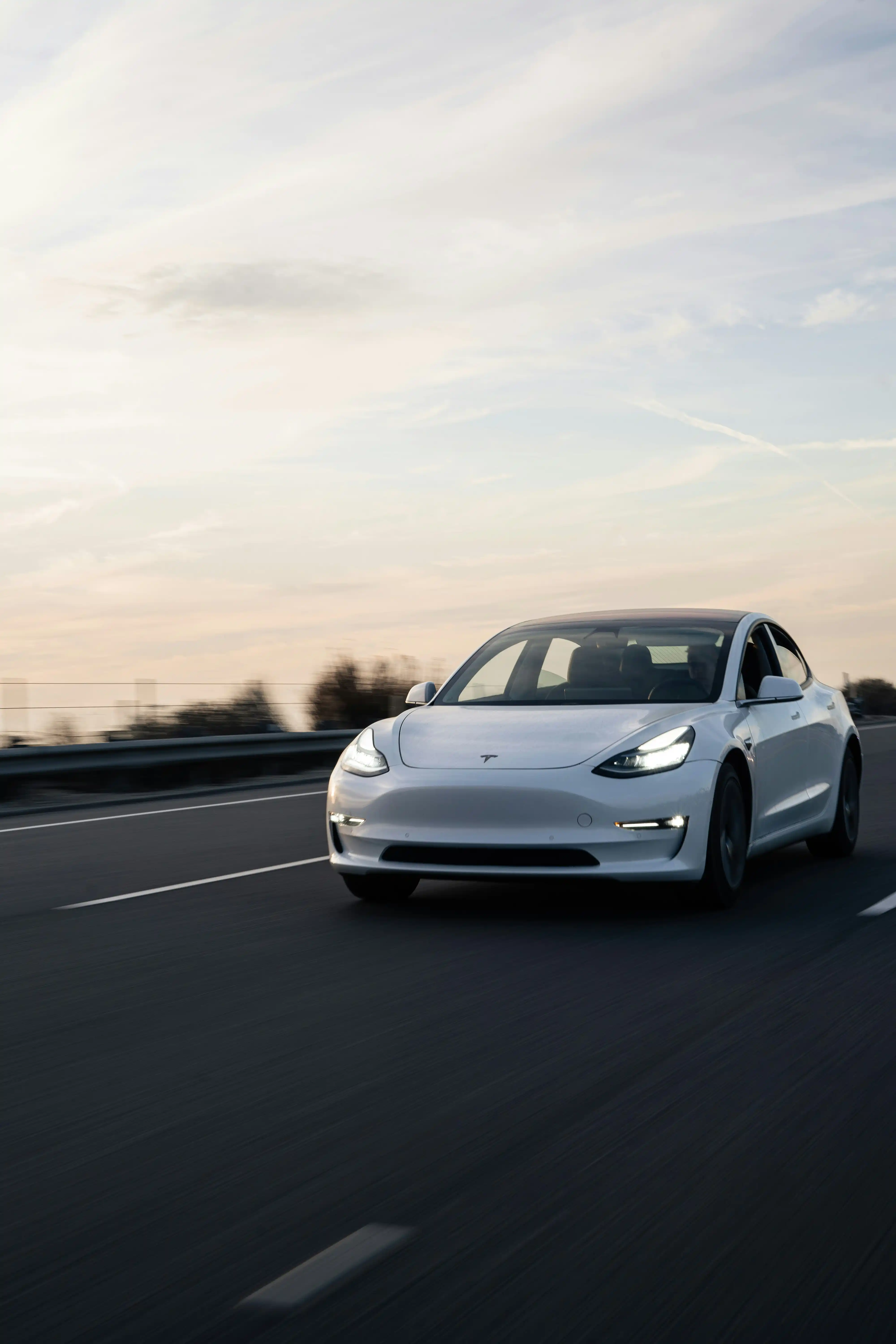 Tesla Model 3 på motorväg i skymning — varje resa loggas automatiskt i Autojournal